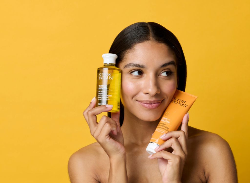 woman holding vitamin c cleansing oil and micro polish wash against her cheeks