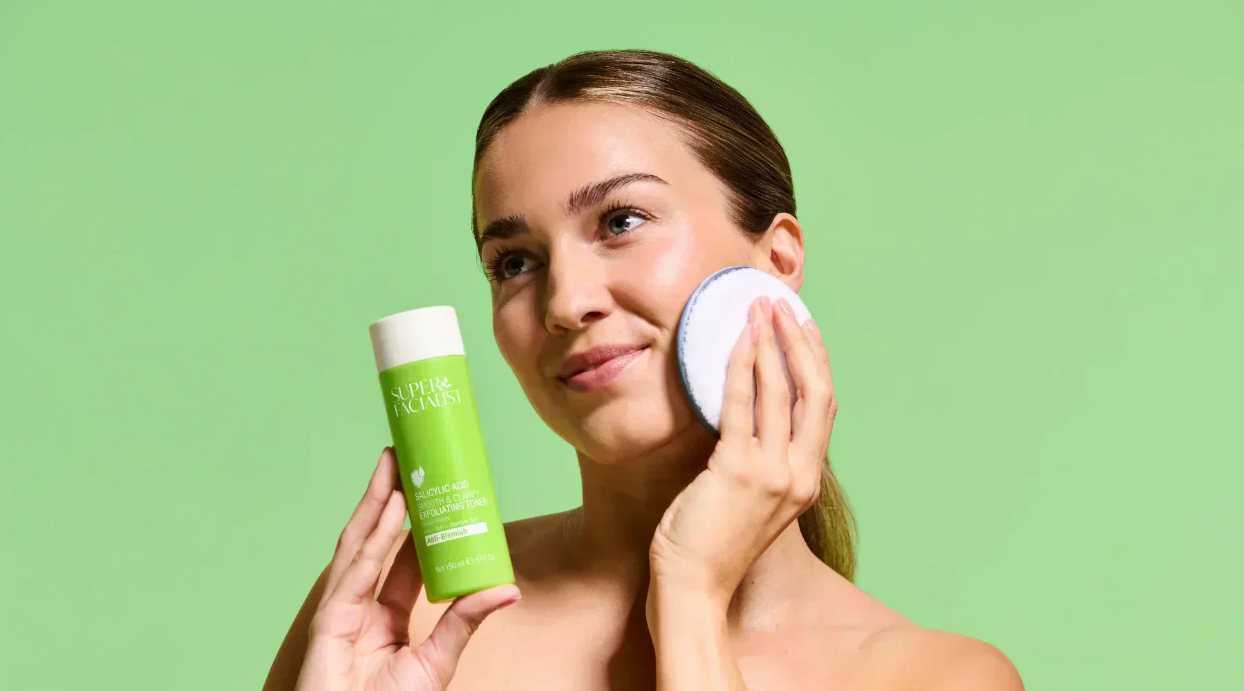 Model applying the  Salicylic Acid Smooth & Clarify Exfoliating Toner 150ml with a reusable cotton pad and holding the product