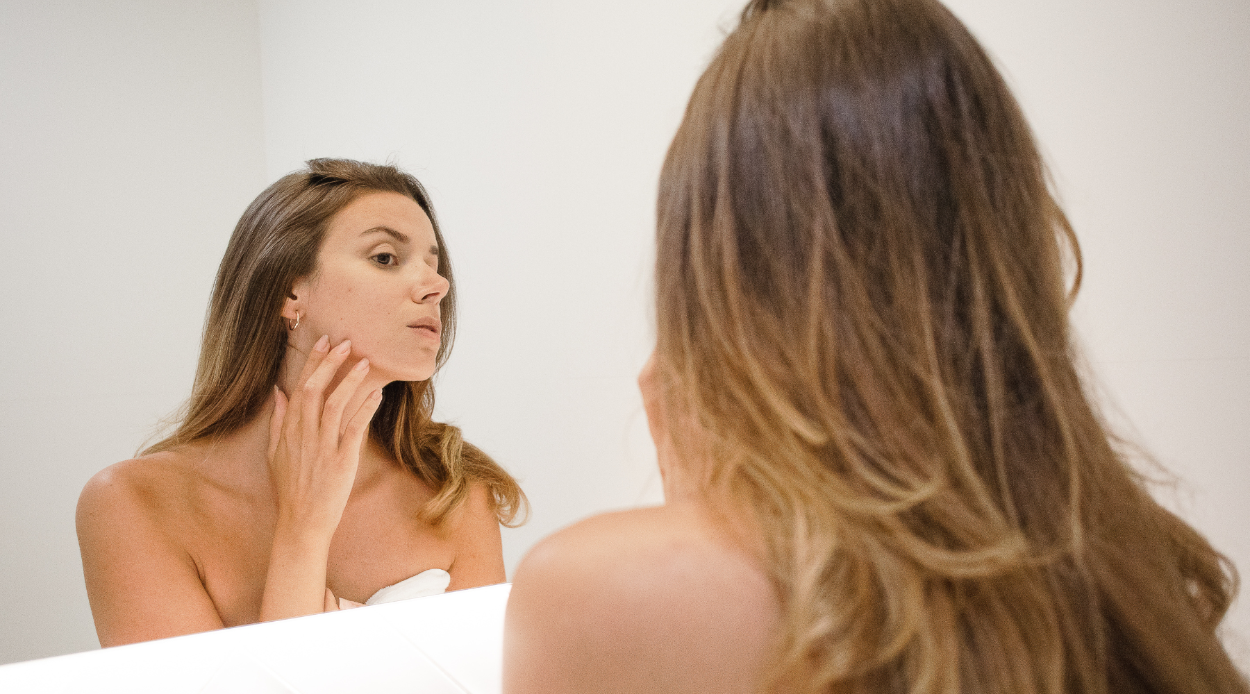 Woman looking in the mirror observing her skin