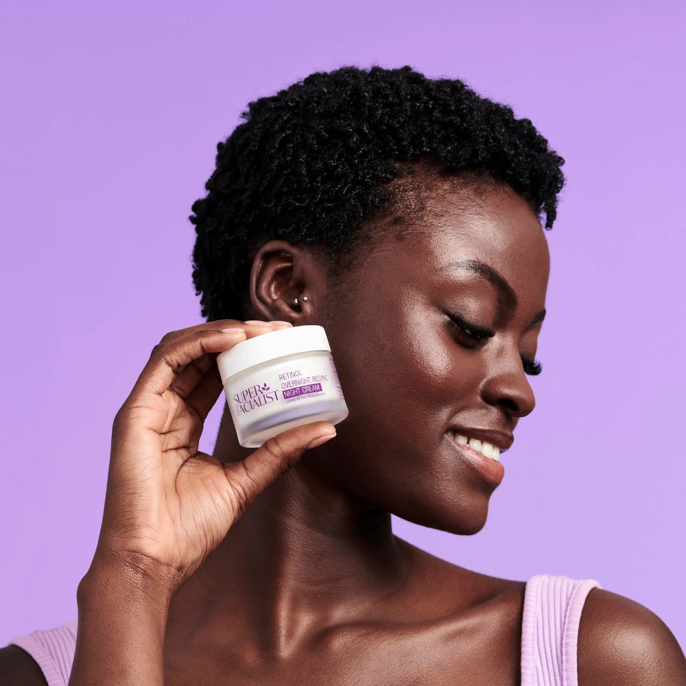 model holding retinol night cream next to her cheek against purple background