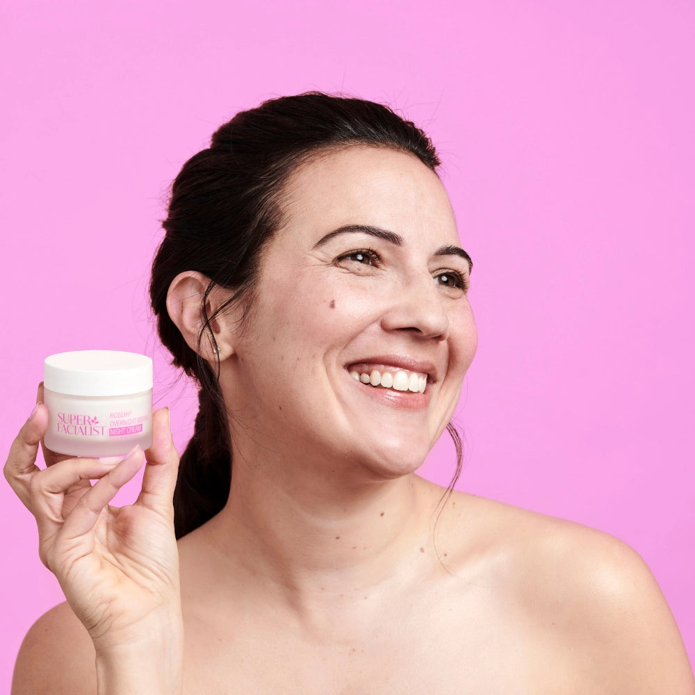 model holding cream jar next to face against pink background