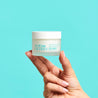 index and thumb finger holding a closed white jar against a blue background