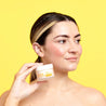 Model headhsot holding Super Facialist Vitamin C SleepSamrt Night Cream jar next to face