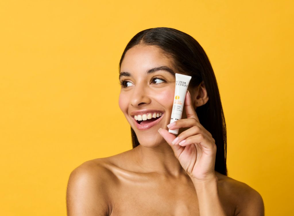woman holding vitamin c eye cream against her cheek