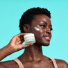 Woman holding a jar of the night cream next to her cheek while looking away.