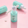 Dropper glass bottle opened with serum dripping out of the dropper on top of a pink table