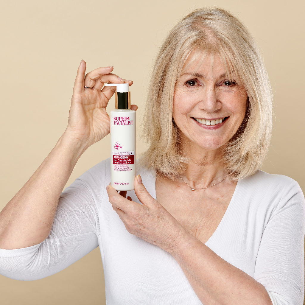 Model holding the Hexapeptide cleansing milk pump bottle with both hands while smiling at the camera
