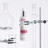 Hexapeptide cleansing milk pump bottle inside a white lab surrounded by glass testing tubes