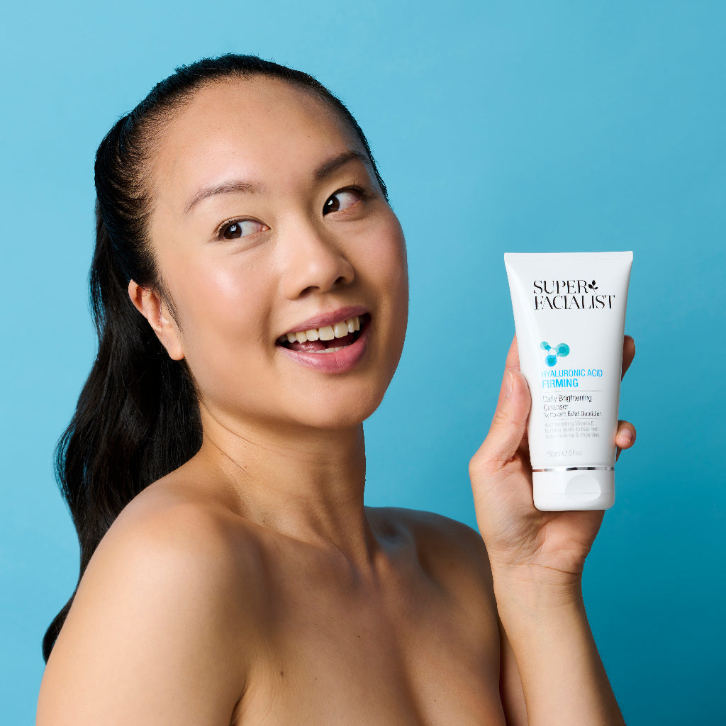 Model holding the Hyaluronic Acid Firming Cleanser tube while looking away in front of blue background