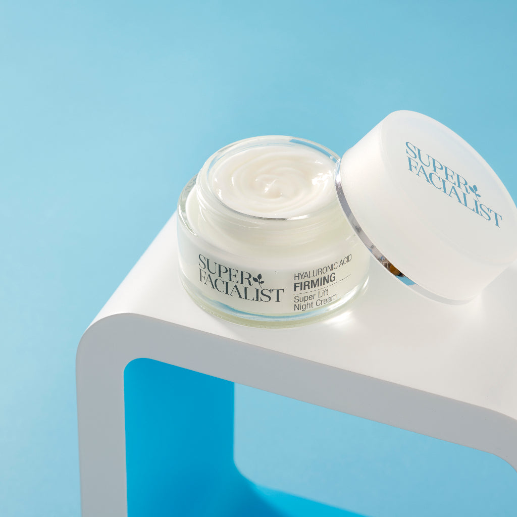 Hyaluronic acid night cream jar opened on top of white square prop against blue background