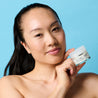 Model holding hyaluronic acid day cream jar under her chin while looking into the camera with blue background