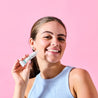 Model applying spot gel onto her cheek with one hand while smiling at the camera