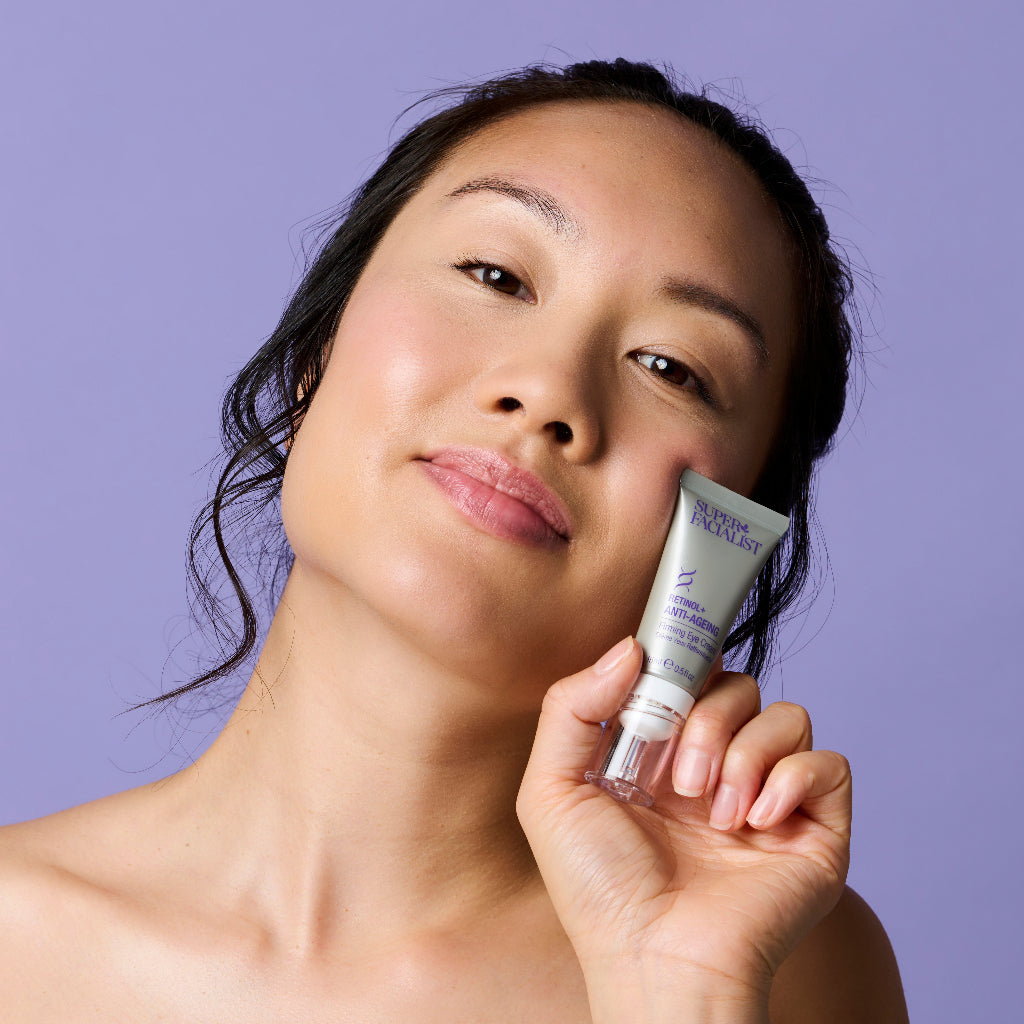 Model holding cream next to her cheek while looking at the camera
