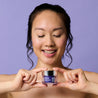 Model holding the retinol night cream jar under her chin with both hands while looking down at the jar