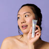 Model holding retinol serum tube next to her cheek while looking away