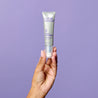 Model holding the retinol serum tube upwards against a purple background