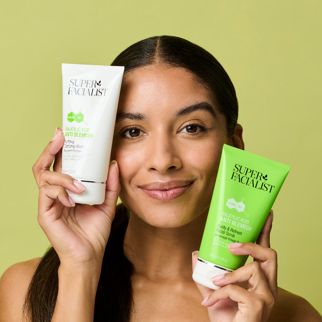 Model holding salicylic acid facial wash and facial scrub on both sides of her face while looking at the camera
