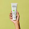 Hand holding salicylic acid clay mask tube upwards against green background