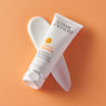 Daily moisturiser tube diagonally placed on orange background  and diagonal cream swatch