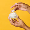 Finger scooping out night cream from the glass jar