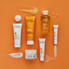 Birds eye view of all super facialist vitamin C products with product textures swatched between the different tubes and jars