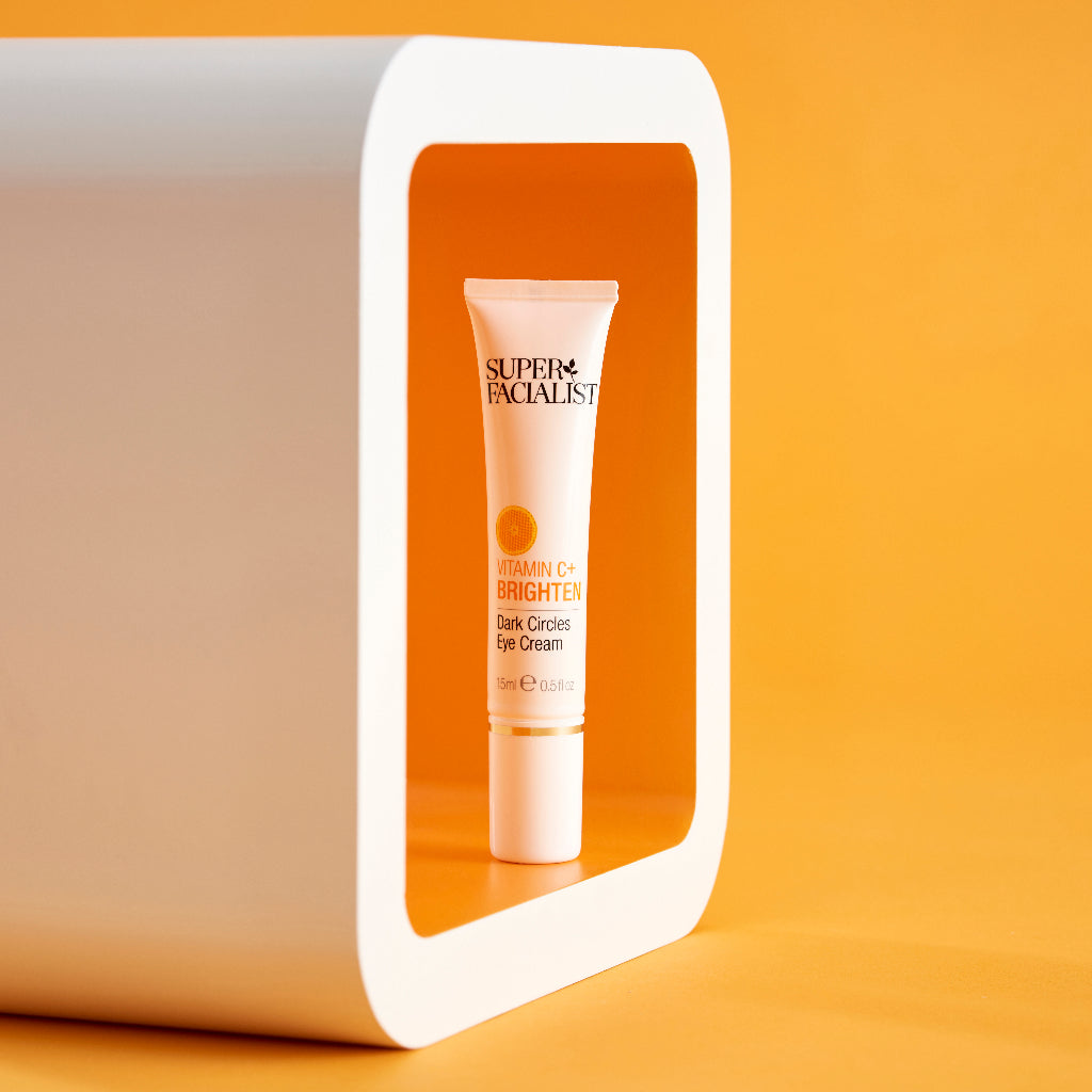Vitamin C eye cream tube inside a white box against orange backdrop