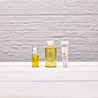 Yellow tube of rosehip facial oil next to yellow bottle of vitamin c cleansing oil next to vitamin c serum tube against a white brick wall and white wooden table